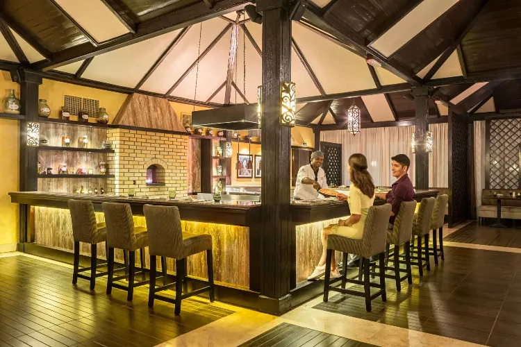 A chef serving pizza to a couple sitting at the La Cucina restaurant in Miramar Al Aqah Resort