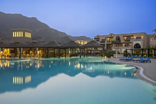 Exterior view of Miramar Al Aqah Resort near the Hajar Mountains, with an outdoor swimming pool